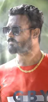 Man in sunglasses and red shirt with gold chain.