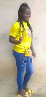 Woman in yellow shirt and blue jeans posing casually.