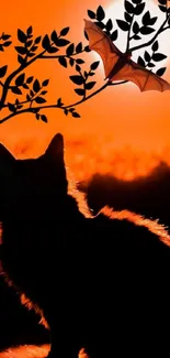 Silhouette of a cat and bat under a tree against an orange sunset.