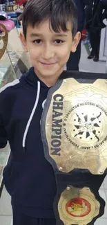 Young boy holding a large trophy and championship belt.