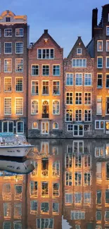 Illuminated Amsterdam canal houses reflecting on water at dusk.