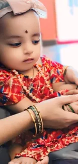 Charming baby in red outfit with bangles, perfect for mobile wallpaper.