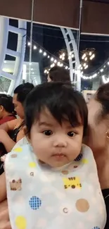 Cute baby in a warm, joyful setting with lights in the background.