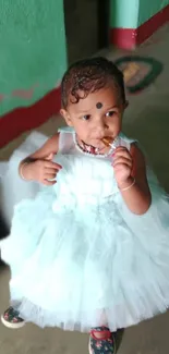 Adorable baby in a white dress standing indoors.