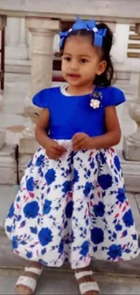 Adorable child in a blue floral dress with stone pillars behind.