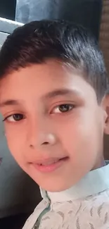 Charming young boy smiling in casual attire under soft lighting.