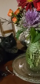 Black cat with floral vase displaying colorful blossoms on a table.