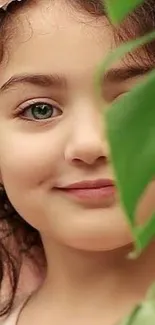 Child peeking behind a green leaf, smiling gently.