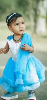 Charming little child in a blue dress standing outdoors.