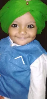 Smiling child in green turban and blue vest.