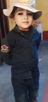 A stylish child in a dark outfit and beige hat indoors.