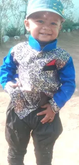 Smiling boy in patterned vest with blue accents standing outdoors.