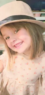 Smiling child in a beige hat and floral dress indoors.