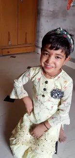 Child wearing pale yellow traditional dress, smiling indoors.