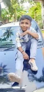 Child sitting on car, surrounded by green foliage.