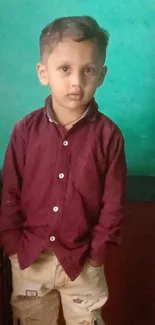 Portrait of a young boy against a teal and maroon background, hands in pockets.