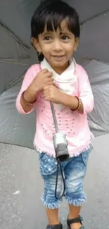 Child with pink outfit holding grey umbrella.