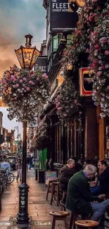 Busy city street with flower baskets and outdoor cafe.