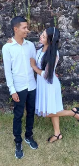 Charming couple in elegant attire by a rustic stone wall.