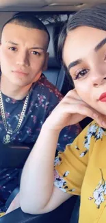 Smiling couple in a car selfie with bright yellow and floral patterns.