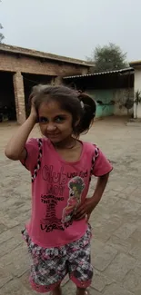 Young girl in pink shirt standing in rustic courtyard.