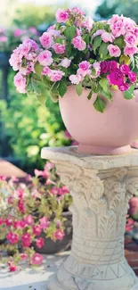 Pink flowers in a vase on a stone pedestal in a garden setting.