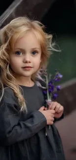 Blonde girl holding purple flowers beside a wooden fence.