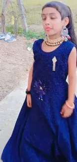 Young girl in elegant blue dress standing outdoors.