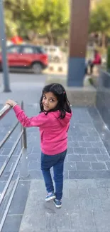 Young girl in a pink jacket walking in a soft-focus urban scene.