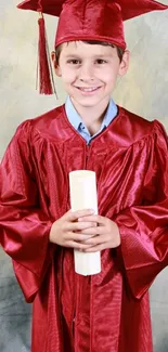 Smiling child in red graduation gown holding diploma.