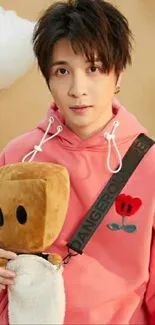 Young person in pink hoodie with plush toy against cloudy background.