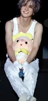 Idol holding a plush toy, wearing a white outfit on stage.