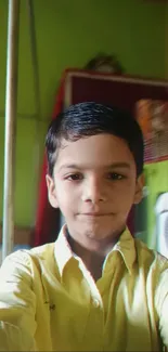 Happy young boy takes a selfie indoors, wearing a yellow shirt.