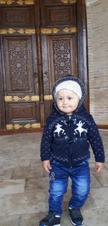 Child in cozy outfit stands by ornate door.