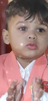 Young boy in a pink suit standing elegantly in a decorated room.