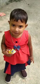 Child in a red dress smiling outdoors.