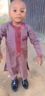 A young child in a brown and red traditional outfit with shiny black shoes.