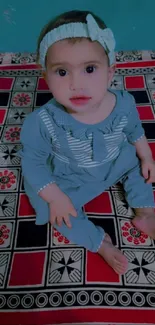 Adorable baby in blue outfit sitting on a vibrant patterned blanket.