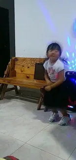 Child dancing indoors with colorful lights and wooden bench.