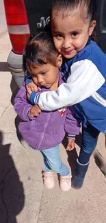 Two kids sharing a warm embrace, smiling outdoors.