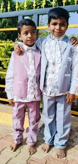 Two smiling children in colorful pastel suits pose outdoors.