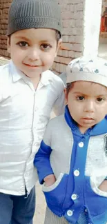 Two smiling kids in cozy blue and white attire with a brick wall backdrop.