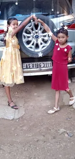 Two children joyfully posing in front of a silver car in a natural setting.