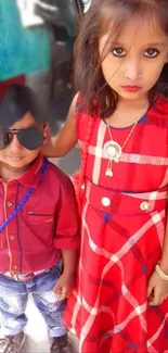 Two children in stylish red attire posing outdoors.