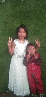 Two children pose peacefully on lush green grass, showing peace signs.