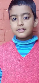 Child in colorful attire against a brick wall.