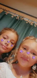 Two smiling kids with a butterfly filter, teal curtain background.