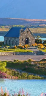 Stone cottage by a lake surrounded by greenery at sunrise.