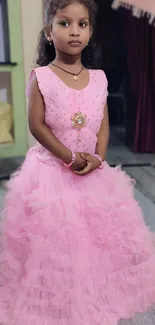 Little girl in a pink ruffled dress standing indoors.