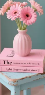 Pink daisies in a vase on pastel books and blue stool.